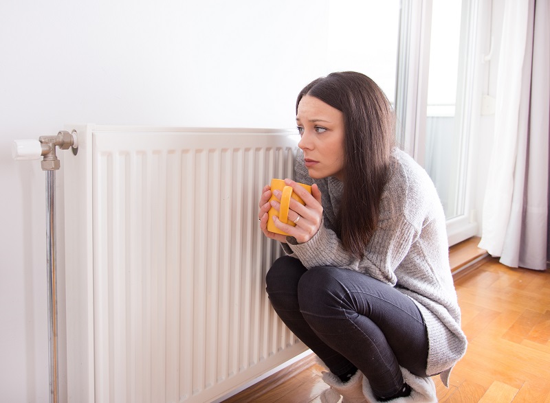 Chica con una taza en las manos pasando frío al lado de un radiador porque posiblemente no funcione correctamente